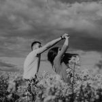 A romantic couple dances in a blooming flower field under dramatic skies in black and white.